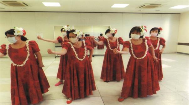 赤の衣装に白い花の髪飾りやレイを身に着けてフラダンスの練習をしている6人の女性の写真