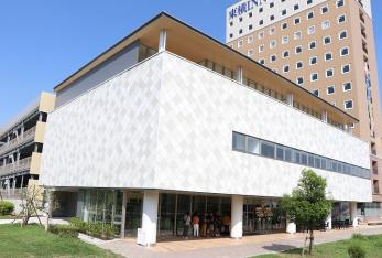 白を基調とした3階建ての三郷中央におどりプラザの入口付近に人が集まっている写真
