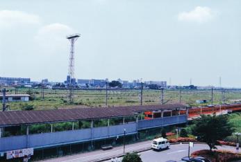 奥に団地が建ち手前に田畑が広がる新三郷駅の駅舎の写真
