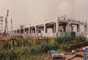 橋が立てられ、左側に3台のクレーン車、手前の空き地に建材が置かれている建設中のつくばエクスプレス三郷中央駅の写真