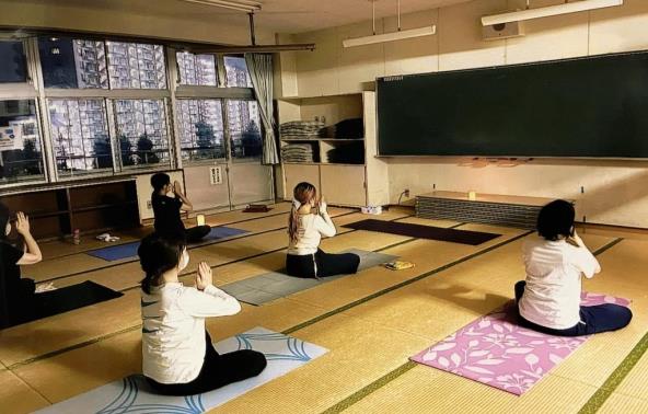 部屋の電気を消してキャンドルライトをつけ、胡坐のような形で足を組んで座り、胸の前で両手を合わせる瞑想のポーズをしている5名の参加者の方々の写真