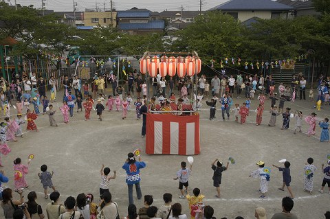 盆踊り大会の中心に設置されたやぐらの上で、和太鼓を叩くメンバーの写真