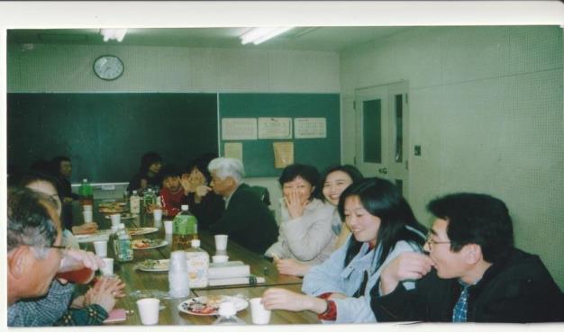 飲み物や食べ物が置かれたテーブルの両側に参加者が座り、談笑している様子を写した写真