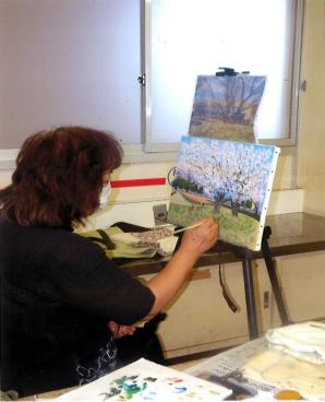 女性が見本を見ながら画架にキャンバスを立てて桜の絵を書いている様子の写真