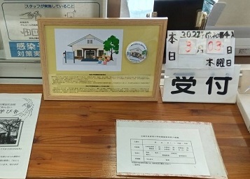 彦成小学校講堂記念館が描かれたイラストと缶バッチが置かれている受付の写真
