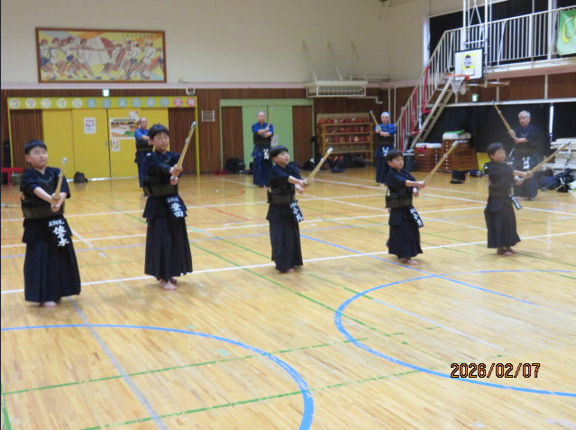 体育館の中で、剣道着と防具を身につけた会員が数組、2人一組で向かい合って竹刀を構え稽古をする様子の写真