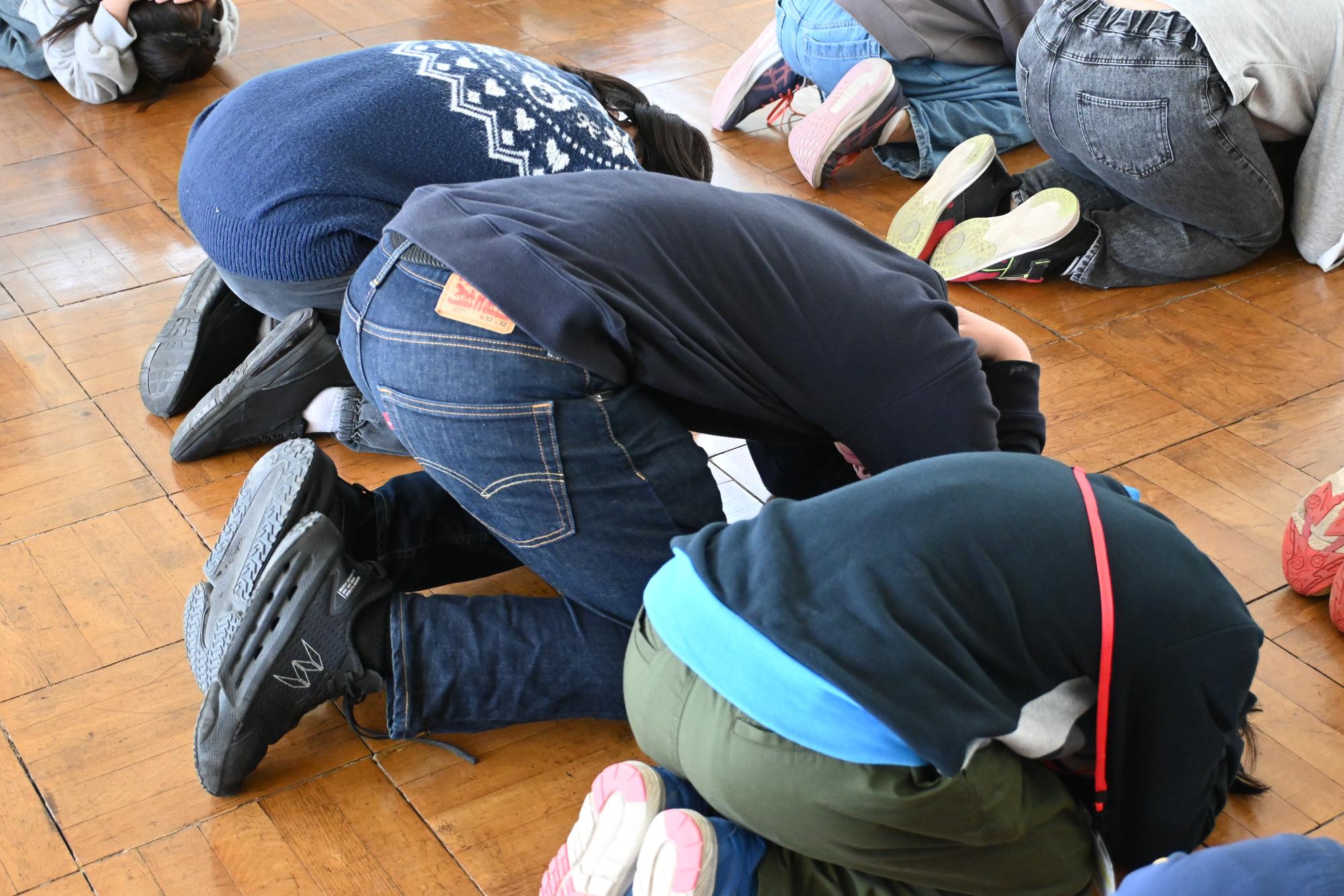 シェイクアウト訓練で「だんごむしのポーズ」をする参加者