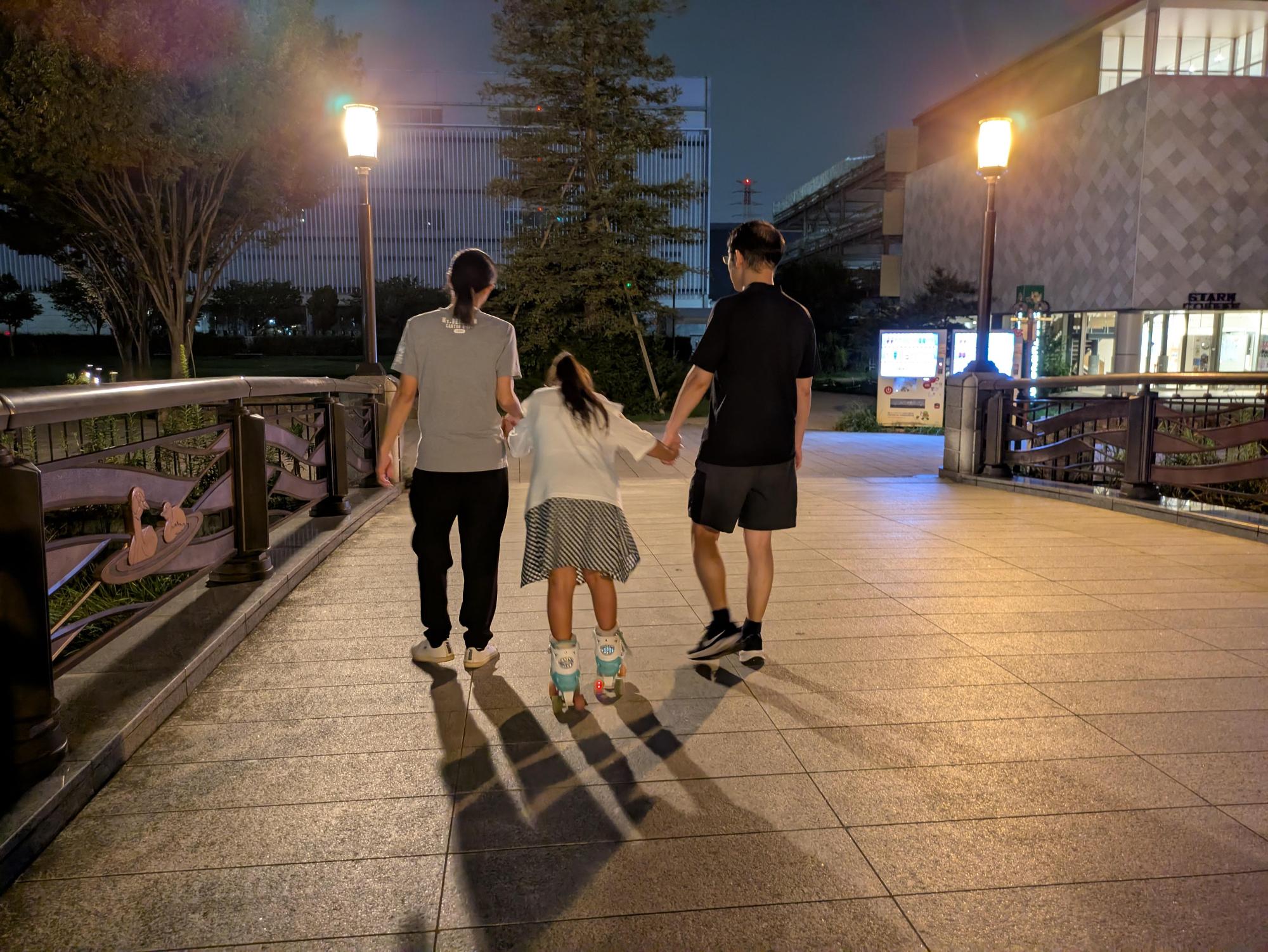 お父さんとお母さんと手をつないでローラースケートをするこどもの様子