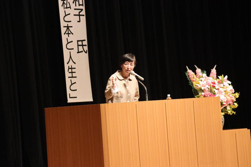 女性がステージ上の演台の前で話している