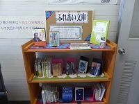 1段目にふれあい文庫の案内、2段目と3段目に本が並べられた彦沢老人福祉センターのふれあい文庫をアップで写した写真