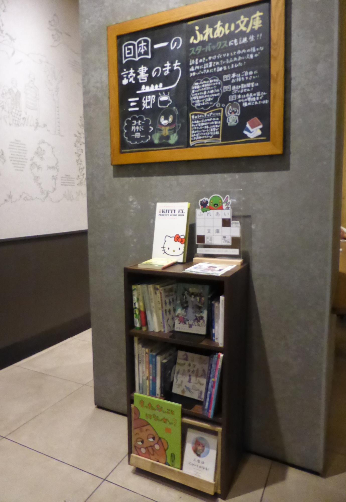 本棚に本が並んでいて本棚の上の黒板に日本一の読書のまち三郷のロゴマークとふれあい文庫について書いてある写真