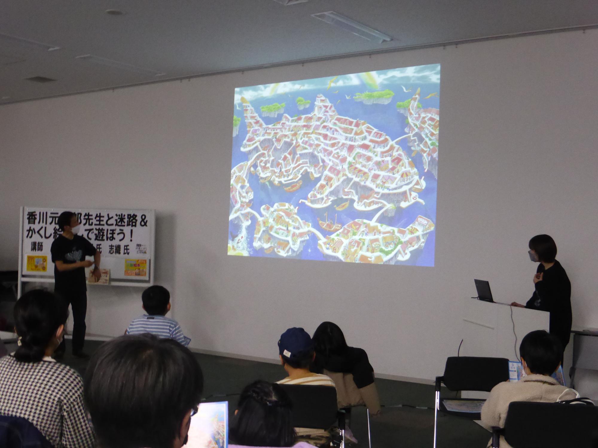 観客の前の壁にサメの形の迷路が映し出されている写真