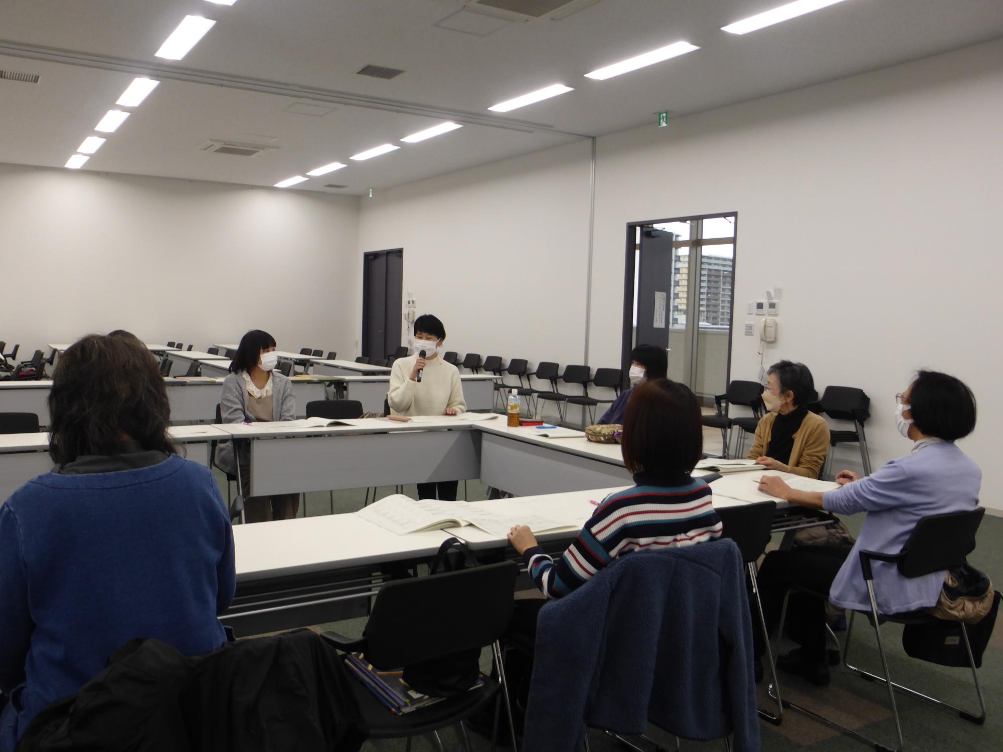 女性がマイクを持って話しているのを周りの人が聞いている写真