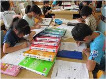 7冊の本が中央に置かれたテーブルに、右側に男子生徒2名、左側に女子生徒2名が座り鉛筆で用紙に書き込みをしている写真