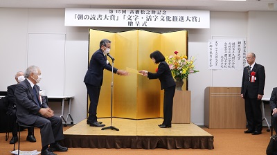 金屏風の前で男性から賞状を受け取る有田るみ子前教育長の写真