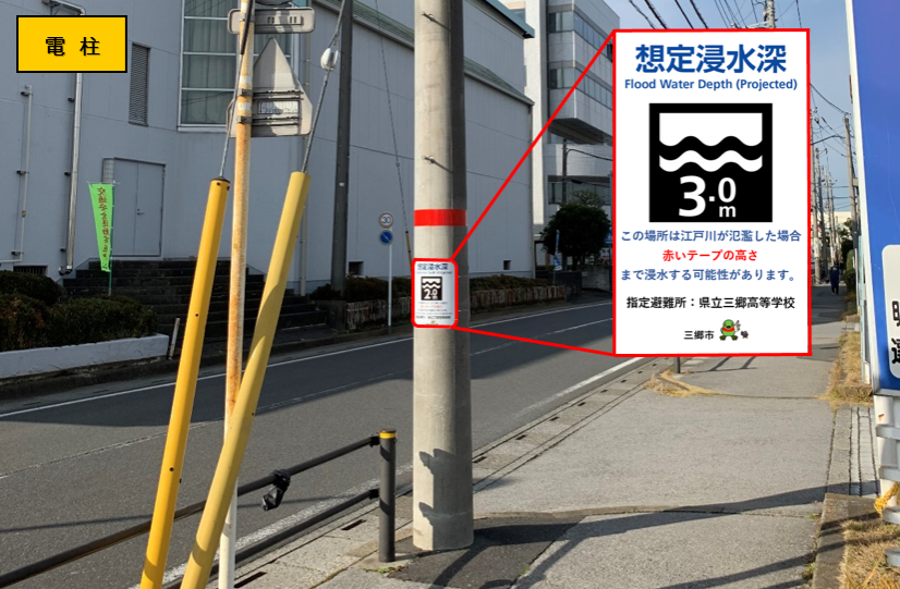想定浸水深3.0メートルの標識が掲げられ、浸水位置を示した赤いテープが巻かれた電柱の写真