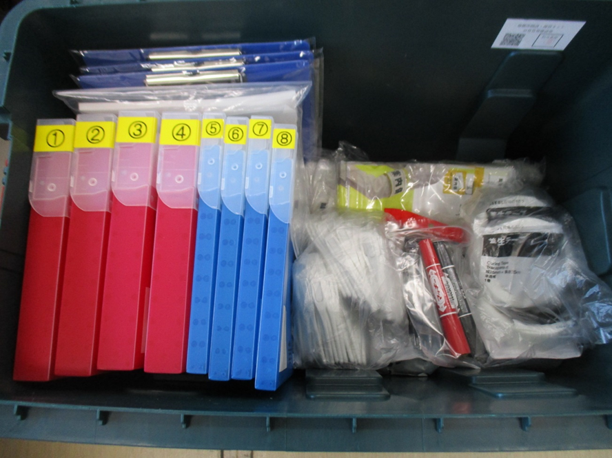 左側に赤と青のクリアケースが並び、右側に養生テープ、筆記用具、下足袋が置いてある写真