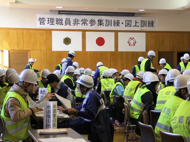 ヘルメットと防犯ベストを着た方々が、各班に分かれて図上訓練を行っている写真
