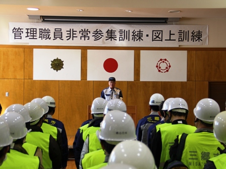 演壇で市長が話をするのを聞いている関係者の後方から撮影した写真